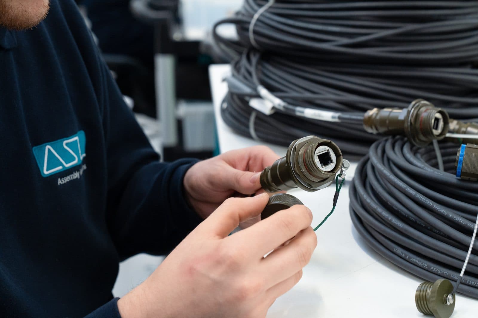 An ASL operator fitting the dust cap to an olive-drab circular connector with an RJ45 data insert, beside coils of shielded data cable with more connectors